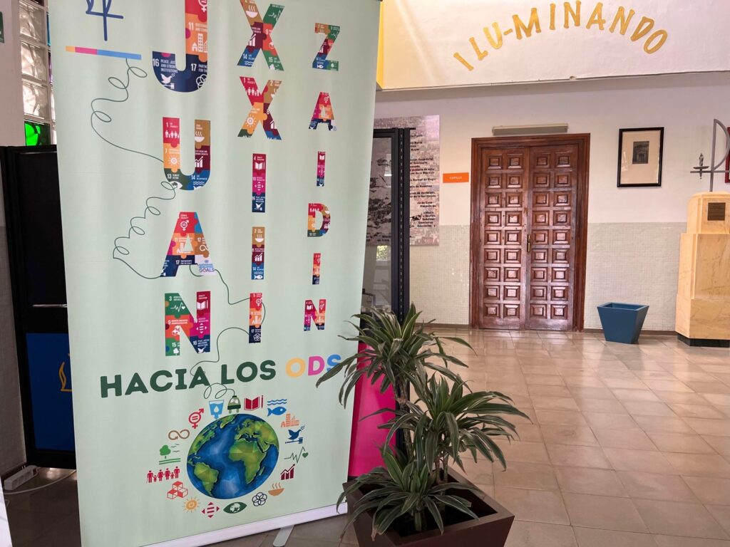 Cartel colorido sobre los ODS en un pasillo con puerta de madera y plantas, texto 