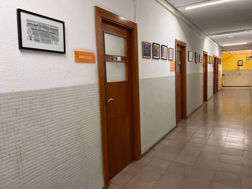 Pasillo de una escuela con puertas de oficina y placas en la pared, incluyendo 