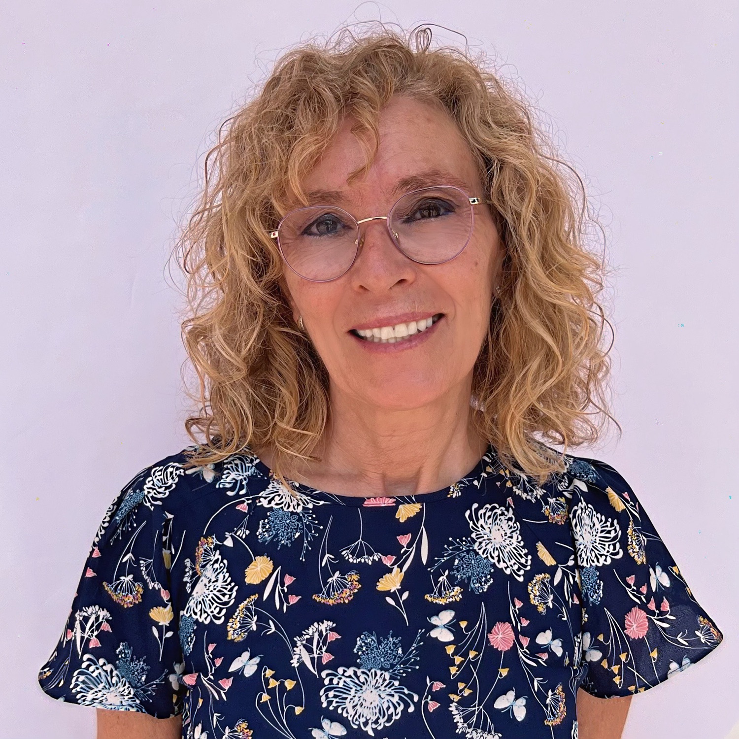 Mujer con cabello rizado rubio, gafas y vestido floral sobre fondo blanco. sonriente.