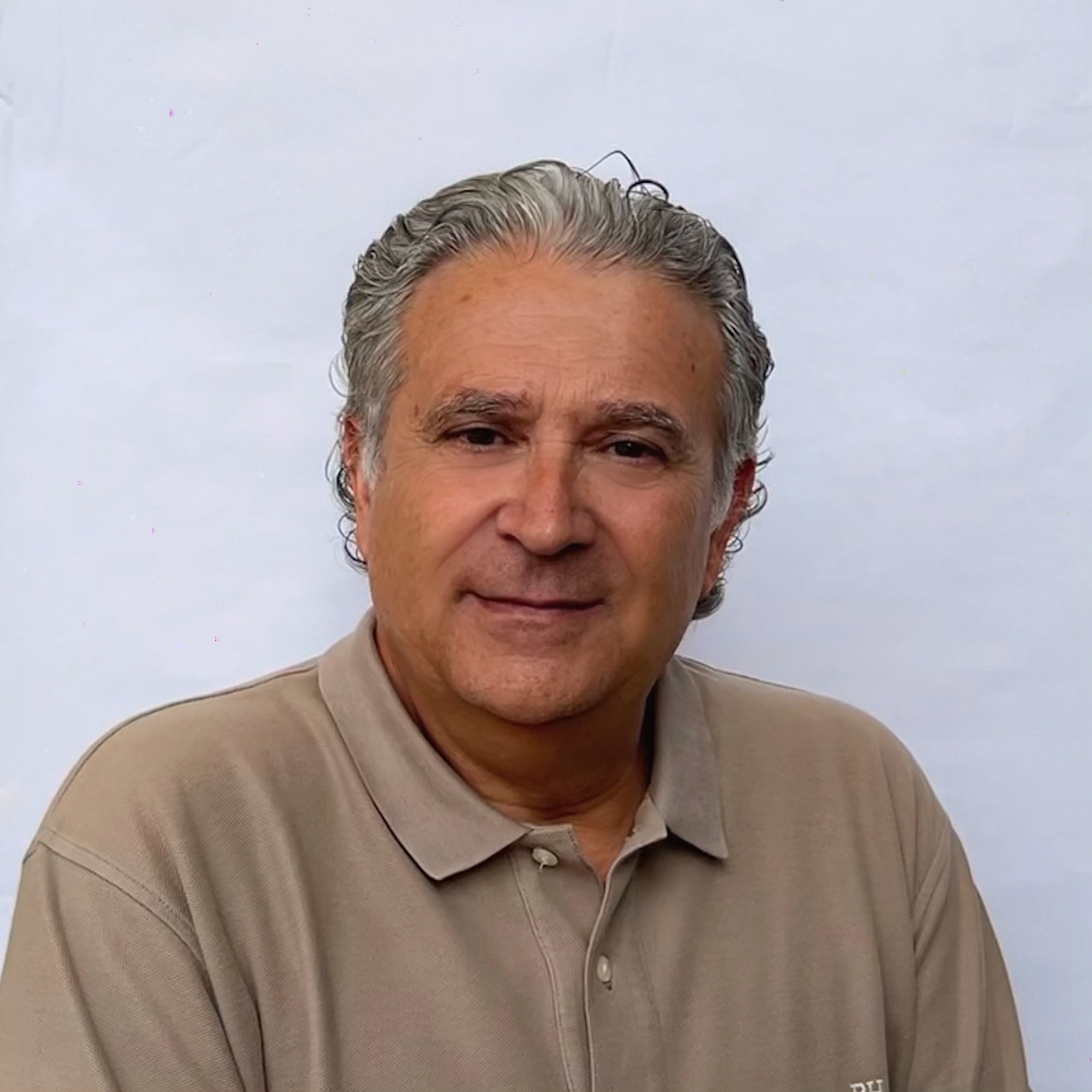 Hombre con cabello canoso, vistiendo una camisa polo beige, posando frente a un fondo claro.