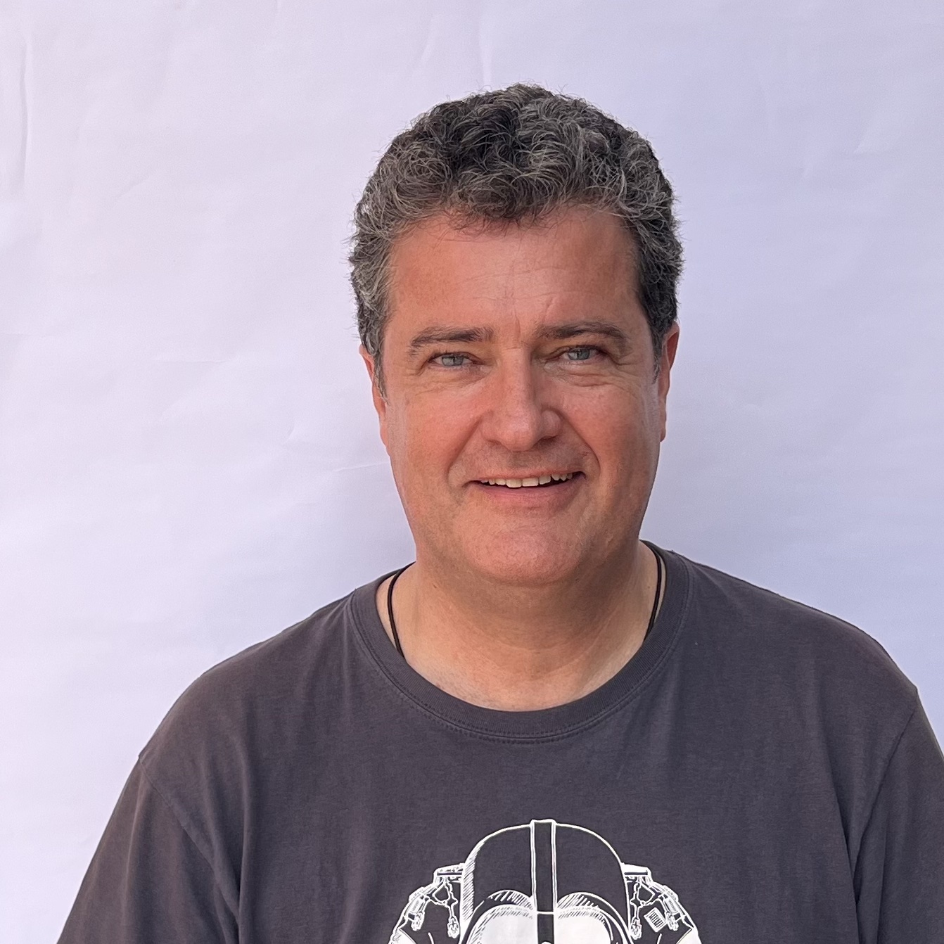 Hombre sonriente con camiseta gris frente a fondo blanco.