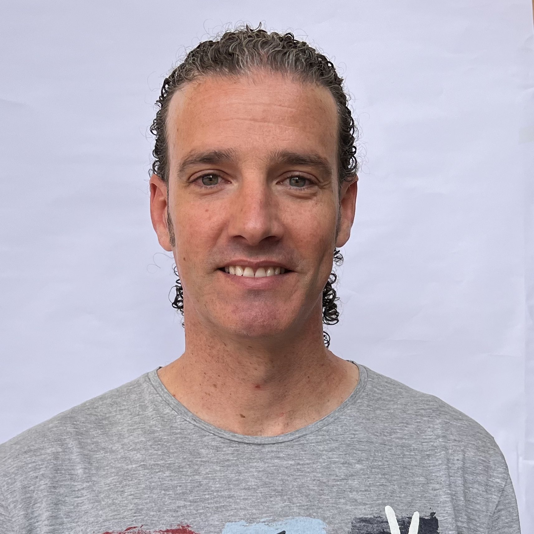 Hombre con camiseta gris sonríe frente a un fondo blanco.