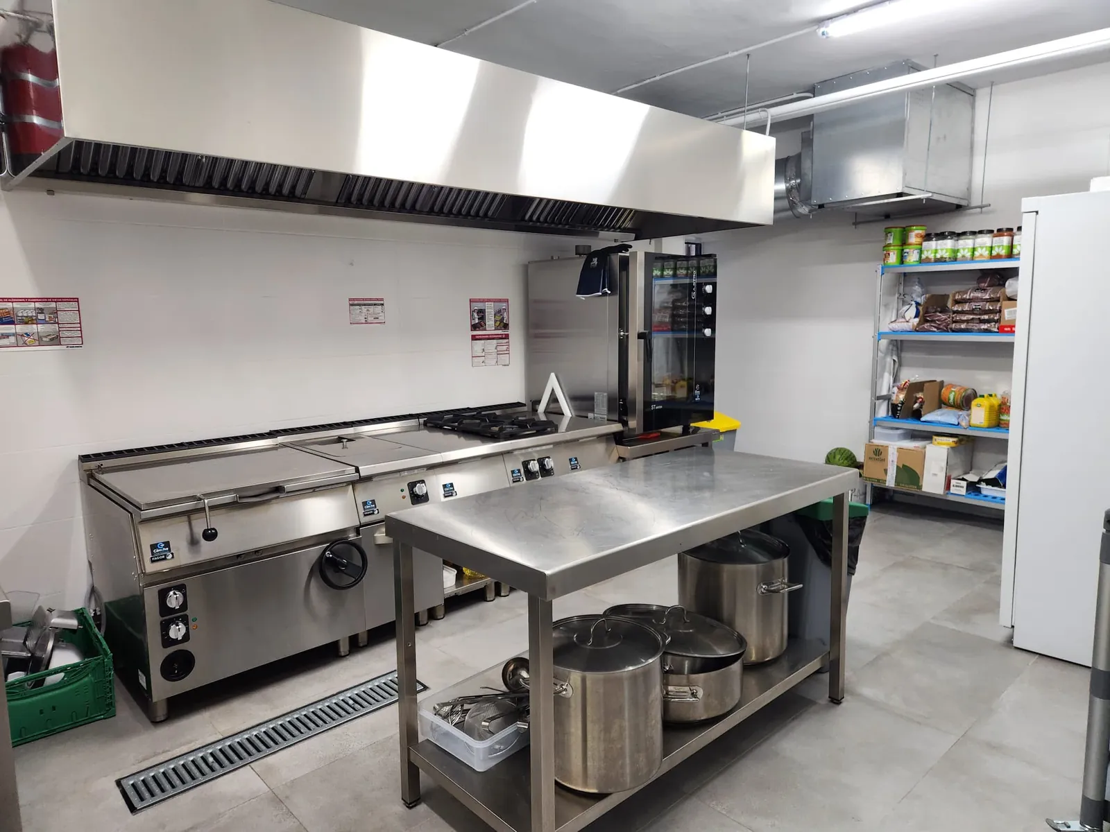 Cocina del comedor escolar de Juan XXIII Zaidín, con fogones industriales, horno y mesa de trabajo de acero inoxidable