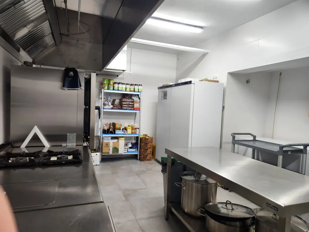 Zona de cocción de la cocina de Juan XXIII Zaidín, con campana extractora, ollas y despensa al fondo